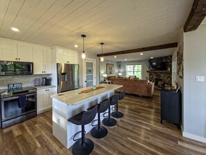 A modern kitchen with a central island, bar stools, and a stone fireplace.