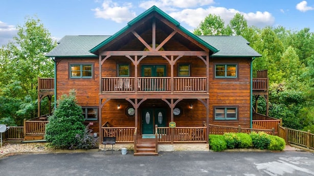 A two-story log cabin with a green roof, wooden balconies, and a front entrance with a green door. - Private 8BR Gatlinburg Cabin w Amazing Views (Gatlinburg)