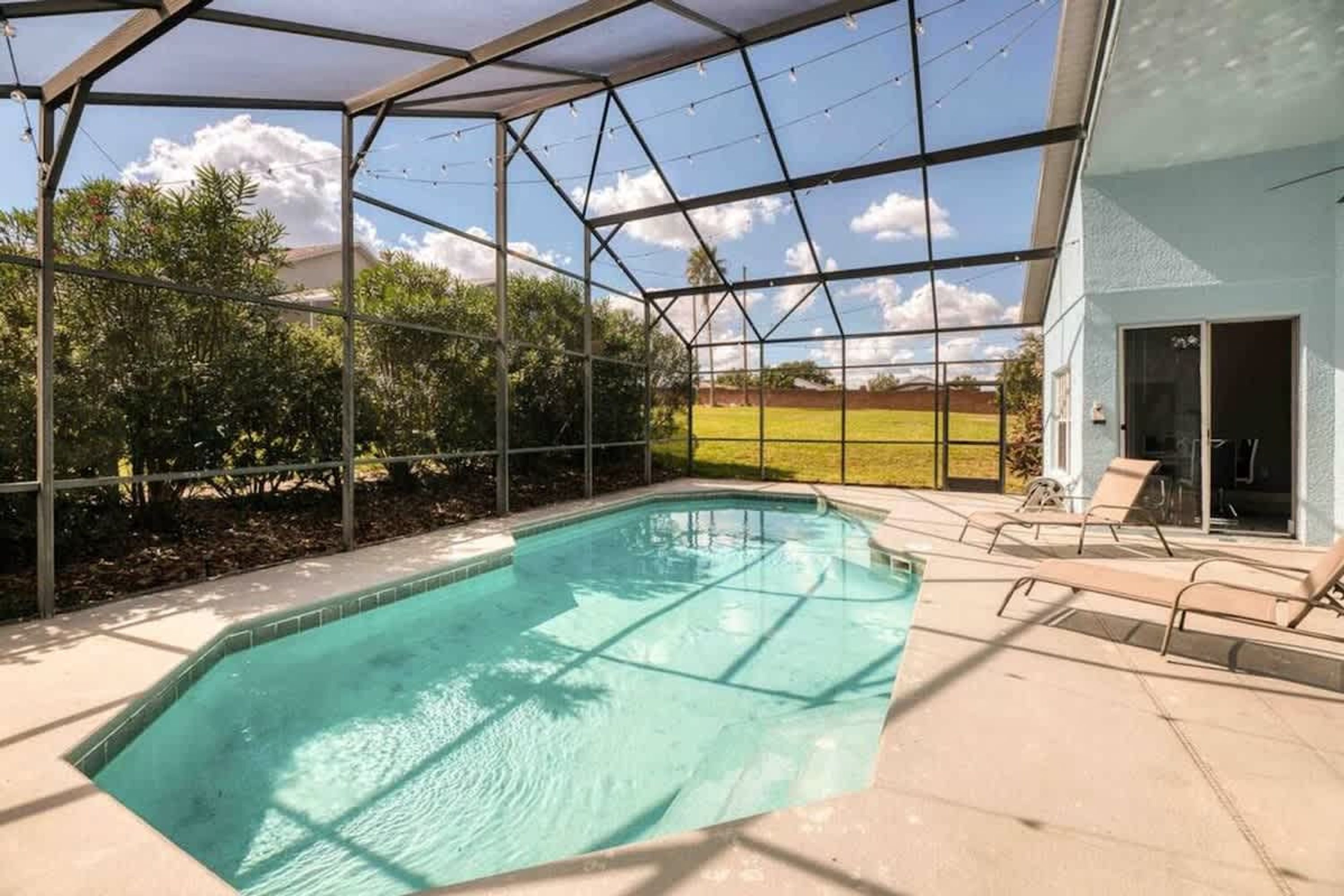 A covered swimming pool with a glass roof, surrounded by a fence, and adjacent to a building with a door.