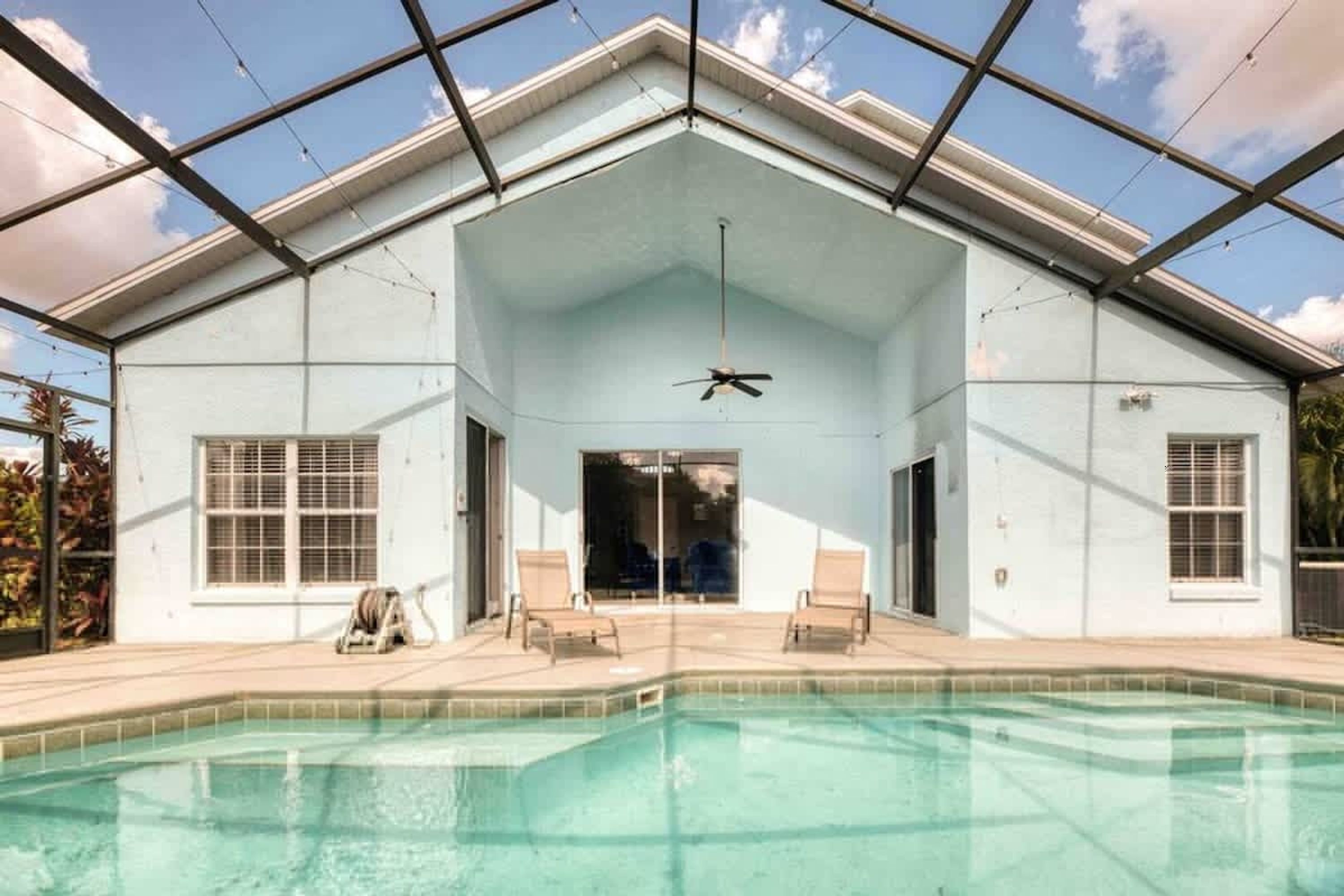 Zona de piscina techada con ventilador de techo, dos sillones de descanso y vista despejada al cielo.