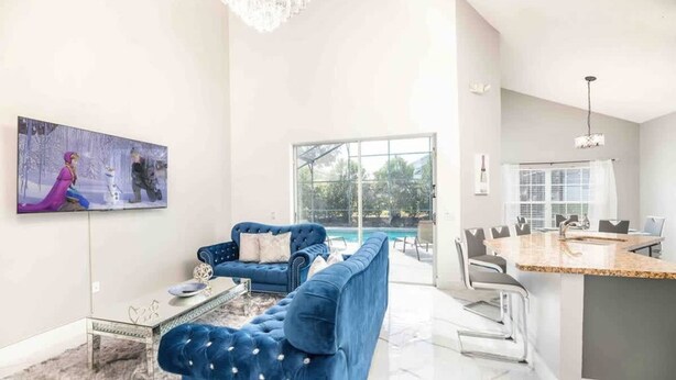A modern living room with a blue sofa, a glass coffee table, and a painting on the wall. - Disney Area 5BR With Pool Spacious and Prime Location (Kissimmee)