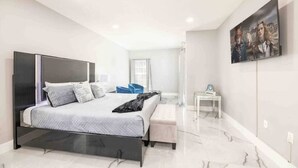 A modern bedroom with a large bed, a bedside table, a small desk, and a wall-mounted TV. - Disney Area 5BR With Pool Spacious and Prime Location (Kissimmee)