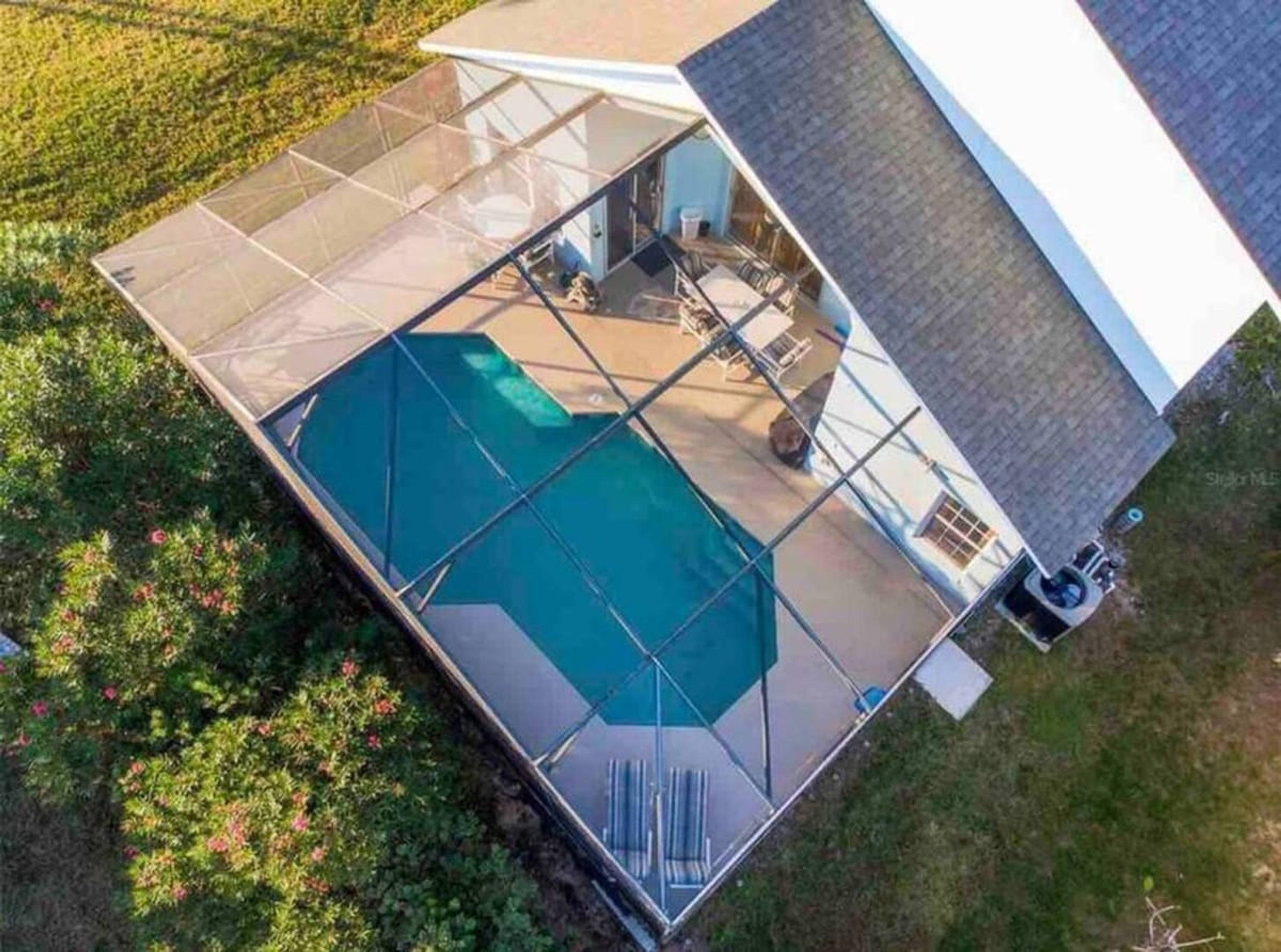 Une piscine entourée d’une structure en verre, elle-même bordée d’une maison dotée d’un toit en pente et d’un garage apparent.