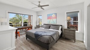 A bedroom with a bed, nightstands, a desk, and a view of the outdoors. - Ocean Breeze Escape South Padre Island (South Padre Island)