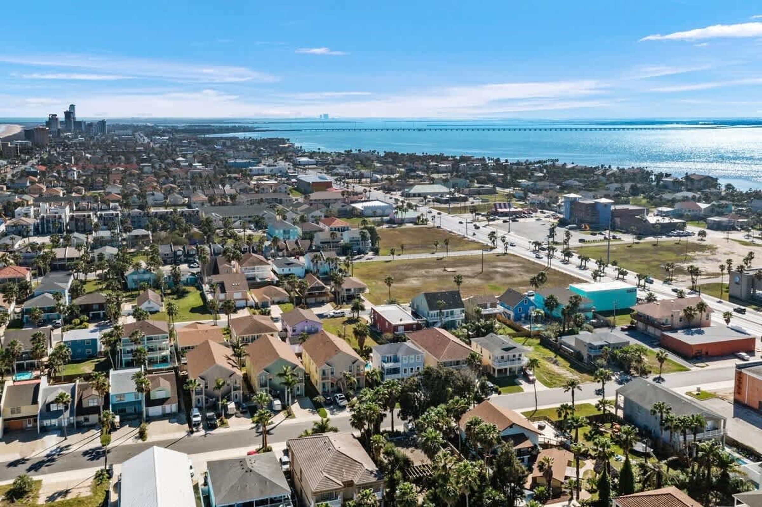 An aerial view of a coastal residential area with houses, a bridge, and a beach.