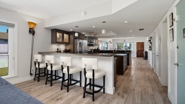 A modern kitchen with bar stools, a large island, and a view of the backyard. - Ocean Breeze Escape South Padre Island (South Padre Island)