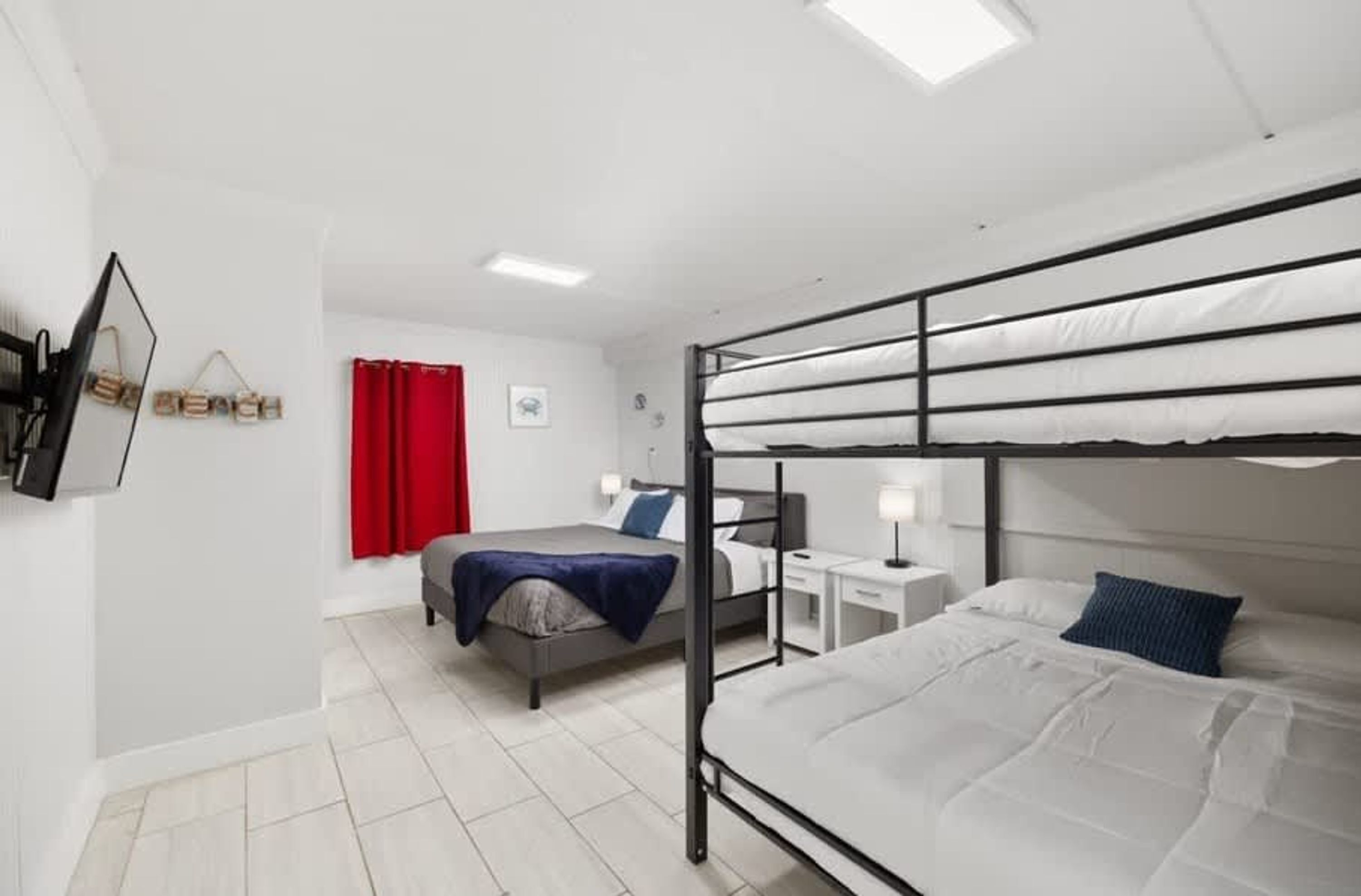 Habitación con literas, un escritorio, una silla, una cortina roja y un cuadro en la pared.