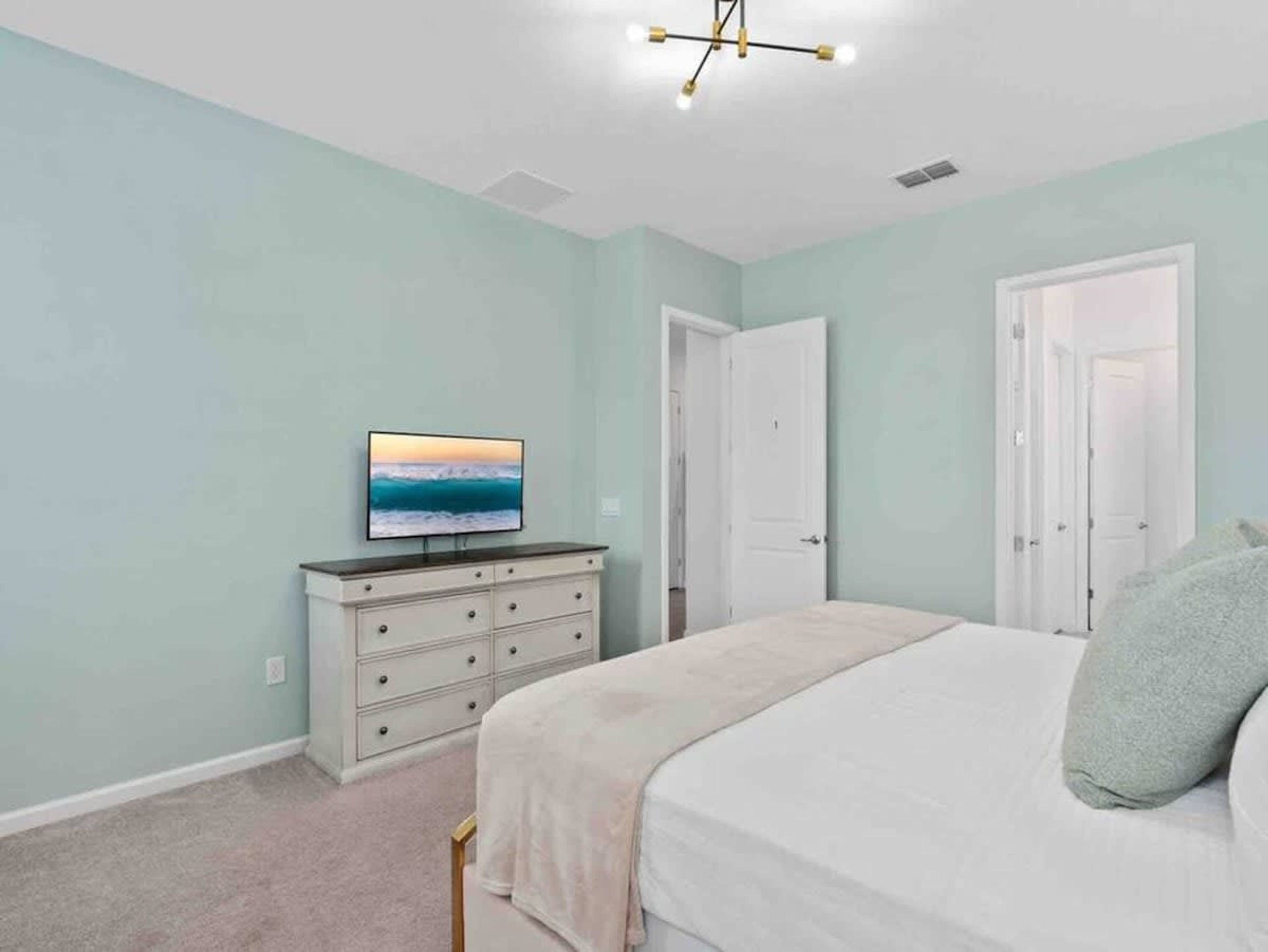A bedroom with a bed, a dresser, a television on the wall, and two doors.