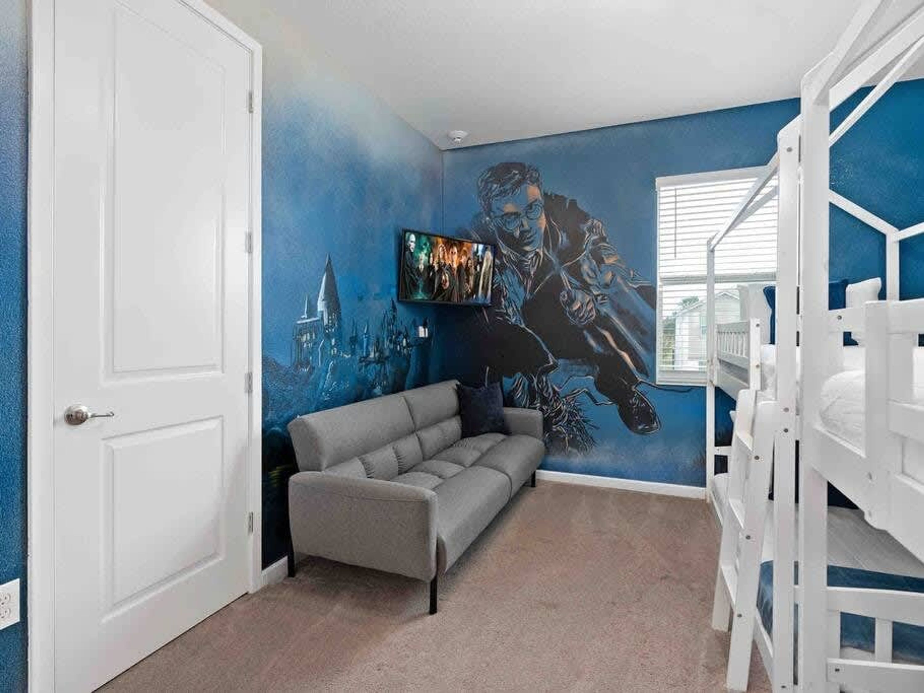 A room with a grey sofa, a bunk bed, and a mural of a castle and a character.