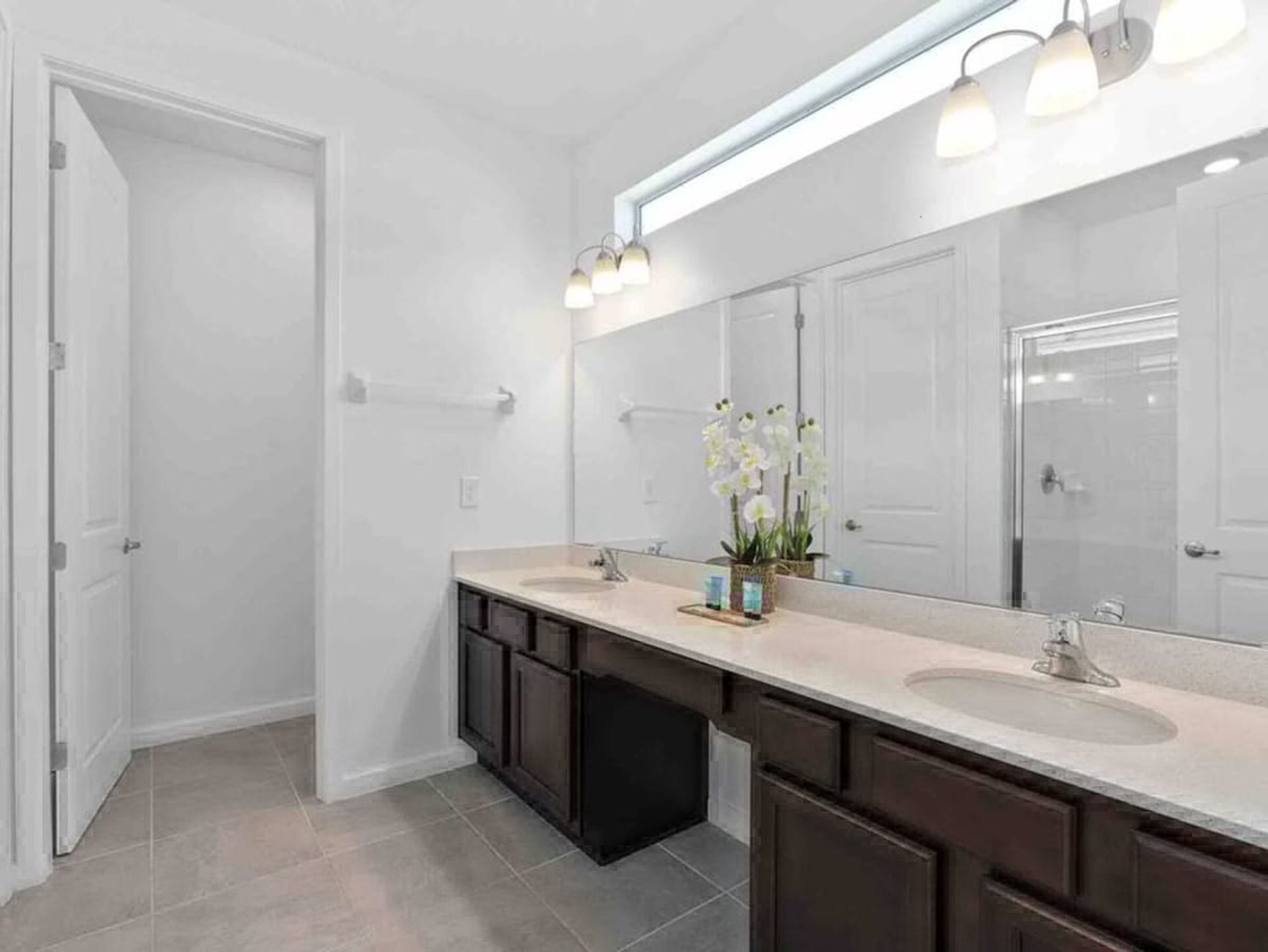 A modern bathroom with two sinks, dark cabinetry, a large mirror, and a light fixture above the mirror.