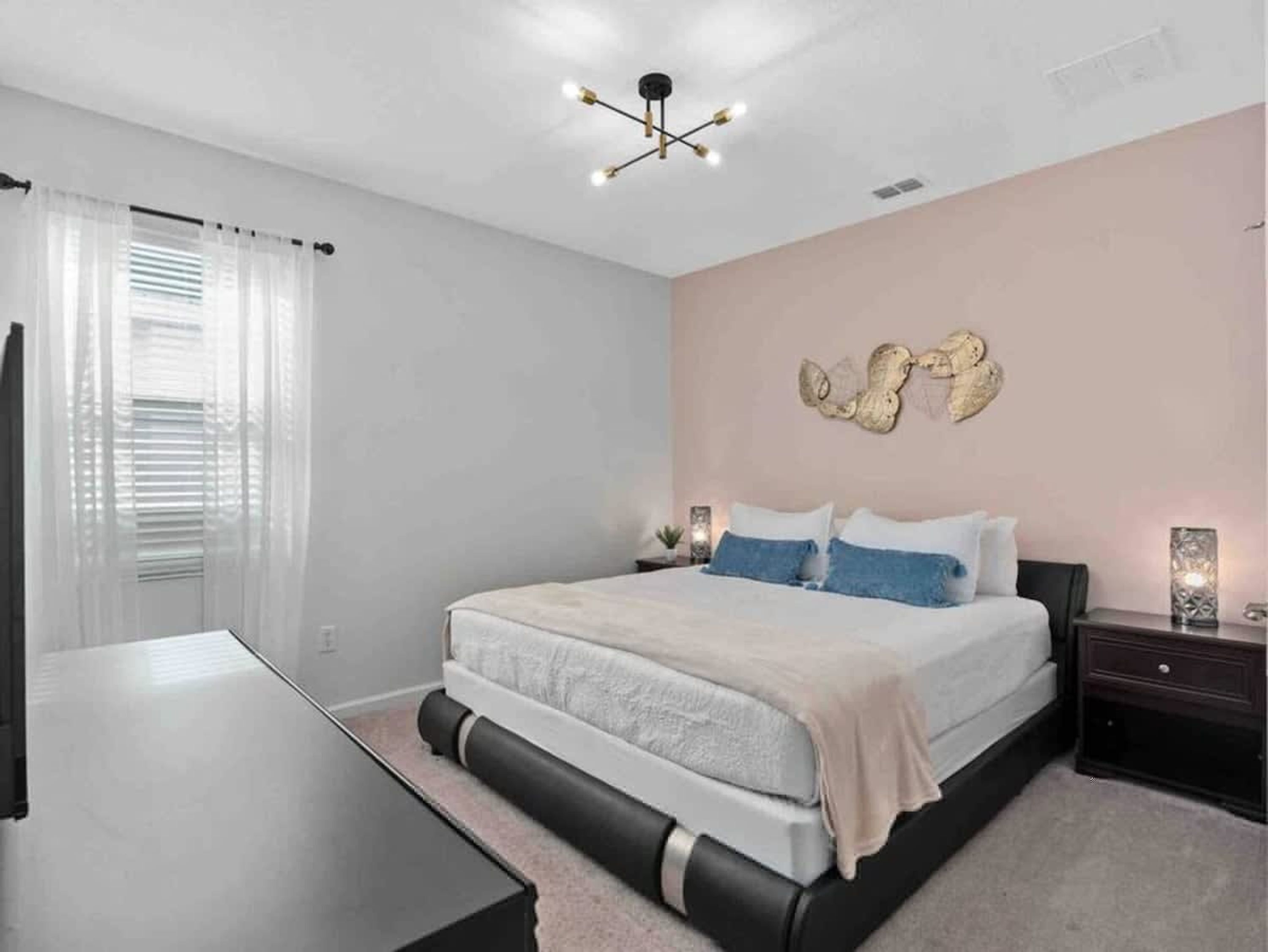 A bedroom with a bed, bedside tables, a ceiling light fixture, and a wall-mounted decorative piece.