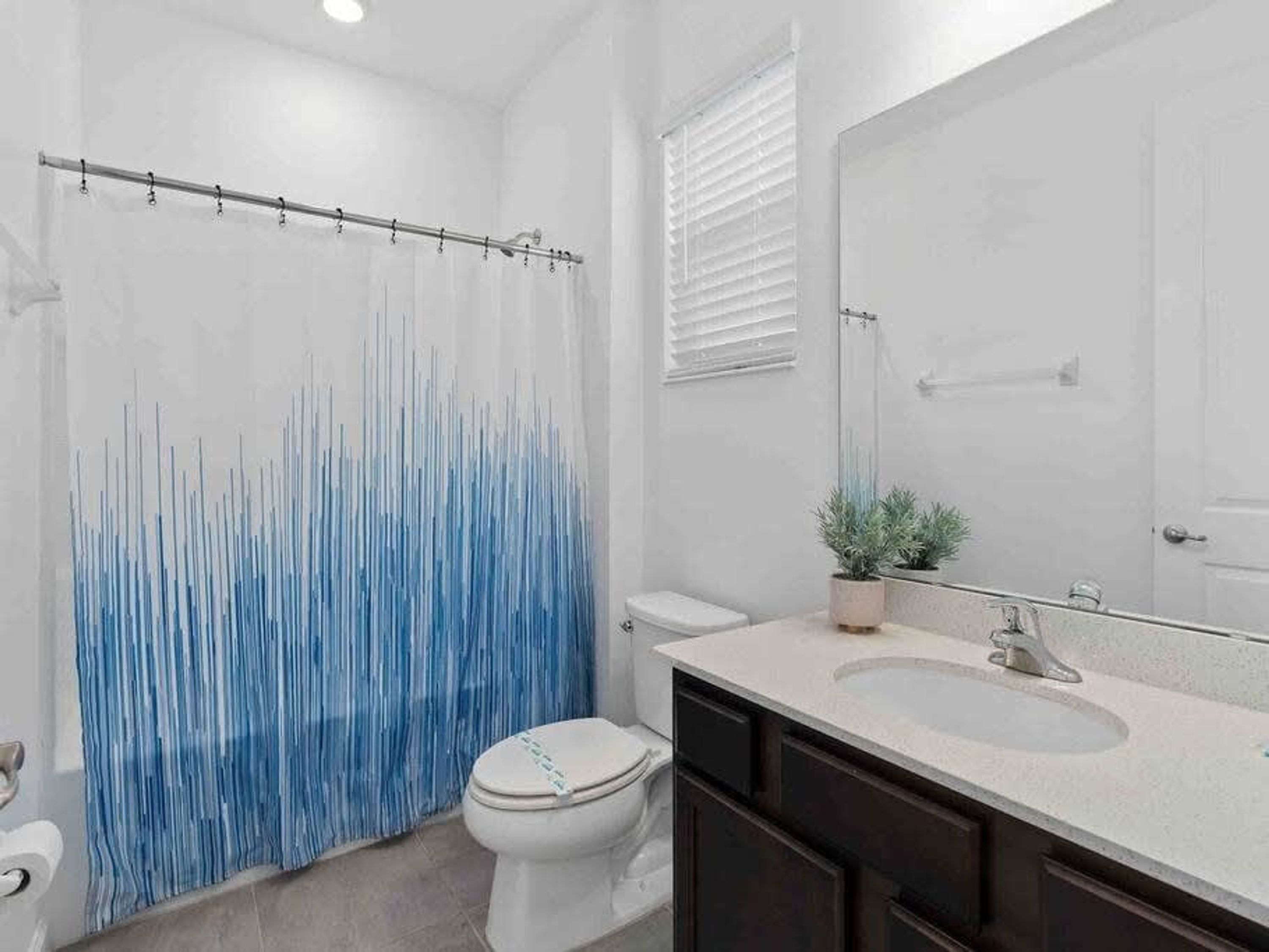 A bathroom with a shower curtain, toilet, sink, and mirror.