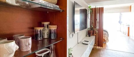 A modern kitchen with wooden shelves, a glass coffee table, and a flat-screen TV.