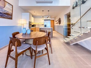 A modern kitchen with a central island, wooden dining table with chairs, and a staircase with glass railings. - Cocotal Penthouse 3 Bedroom Golf View (Punta Cana)