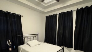 Een slaapkamer met een bed, nachtkastje, plafondventilator en zwarte gordijnen.