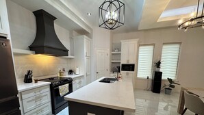 Een moderne keuken met witte kasten, een zwarte afzuigkap en een groot kookeiland met een spoelbak.