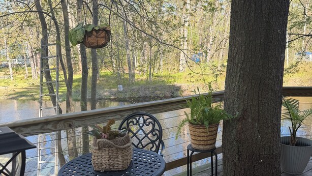A wooden deck with a table and chairs, surrounded by trees and a body of water.