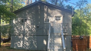 A log cabin with a wooden ladder leading to the door, surrounded by trees and a wooden fence.