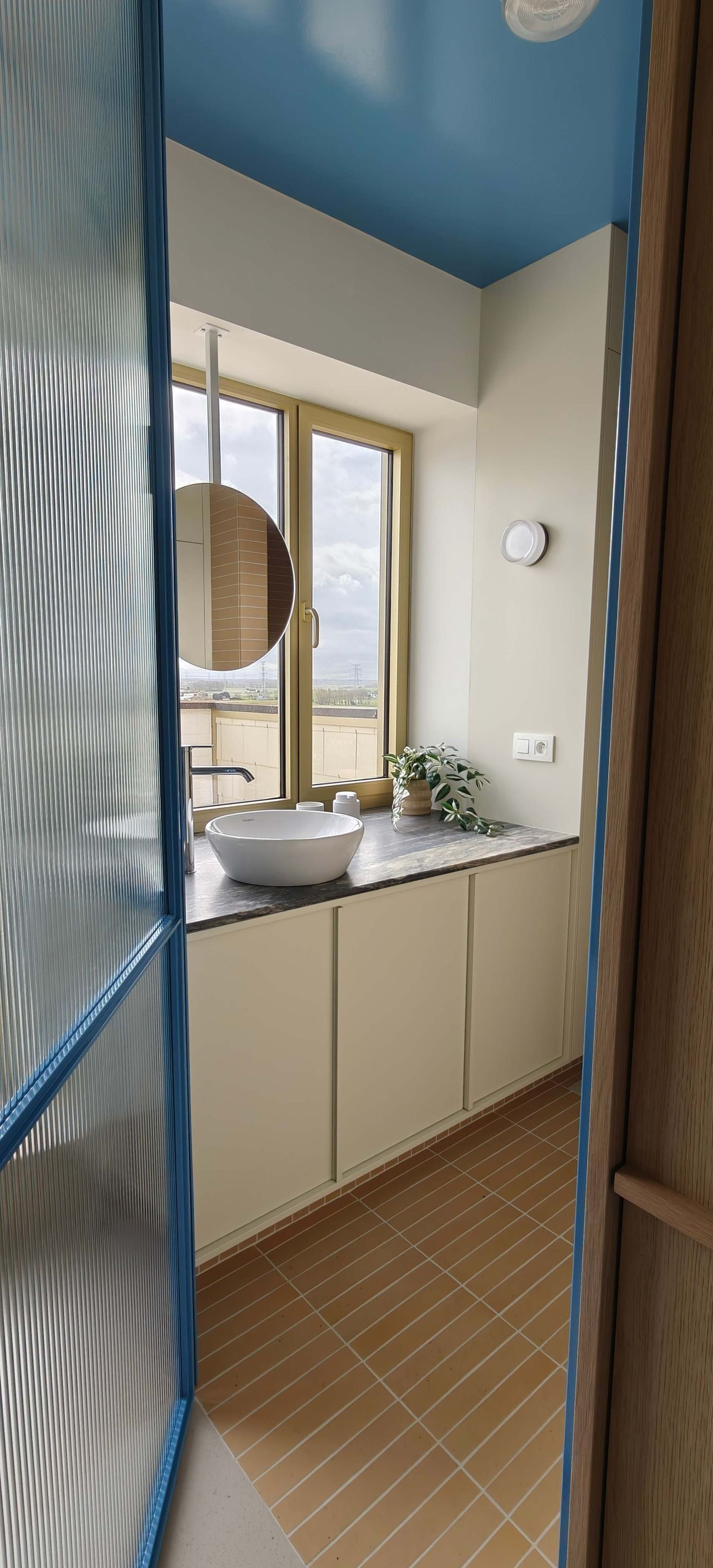 A bathroom with a large window, a white sink, and a mirror.