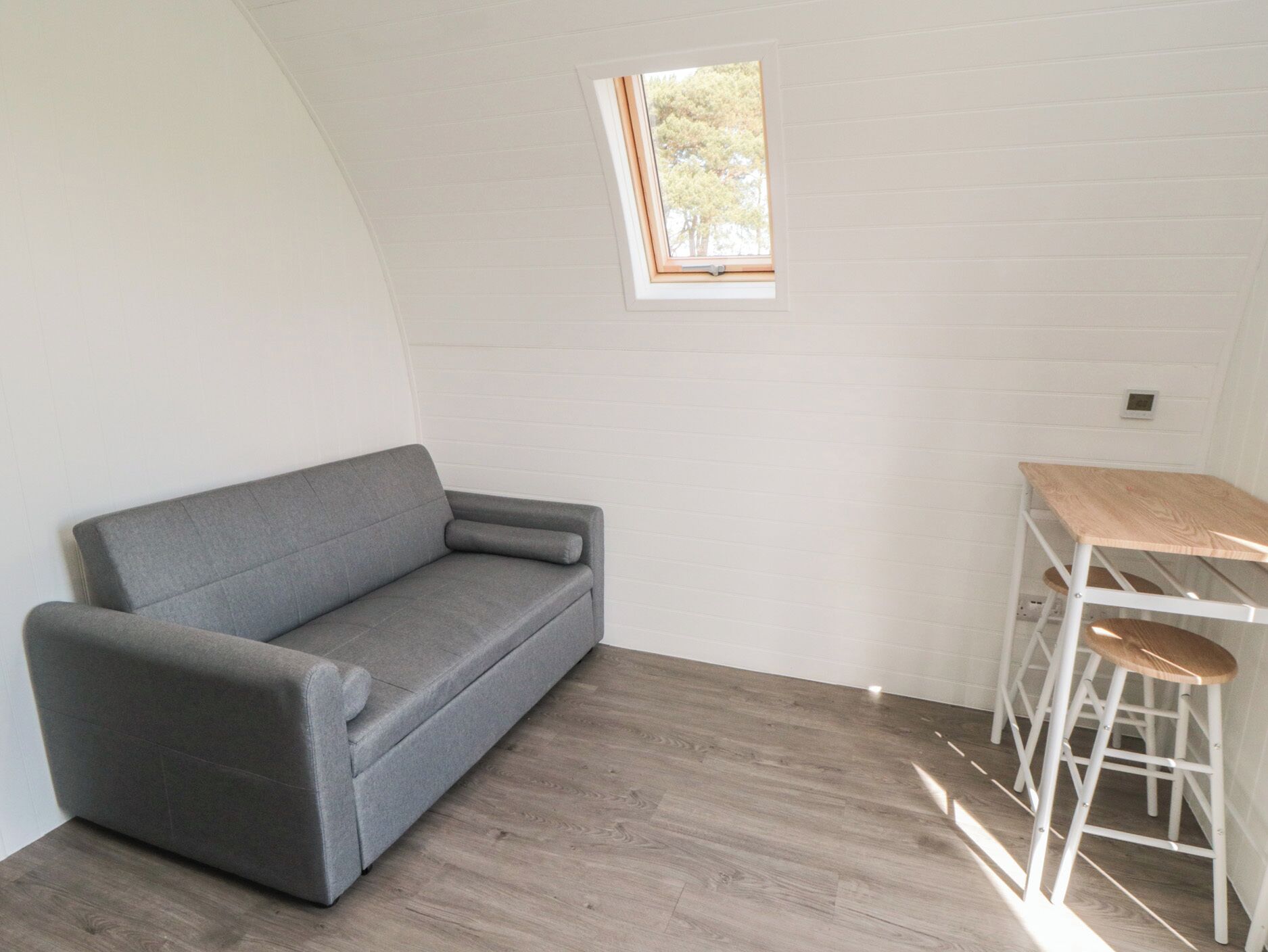 Una habitación con un sofá gris, una mesita con tapa de madera y una ventana que da a vistas de árboles.