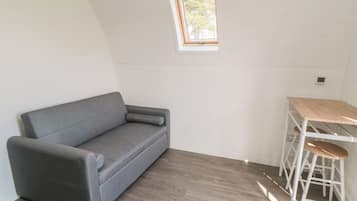 A room with a grey sofa, a small table with a wooden top, and a window with a view of trees.