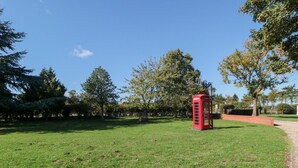 Una cabina telefónica roja en un parque con césped, árboles y cielo despejado.