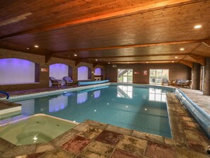 Piscina interior con sillones de descanso y un jacuzzi.