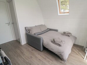 A single bed with a grey headboard and footboard, a window with a view of trees, and a door to the left.