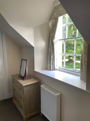 Une pièce avec une fenêtre, un radiateur, une commode et un miroir.