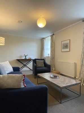 A living room with a sofa, armchair, coffee table, and a hanging light fixture.