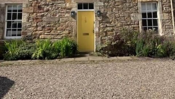 A stone building with a yellow door, multiple windows, and a gravel driveway. - No 2 Stable Yard, Wemyss Castle Estate (Kirkcaldy)