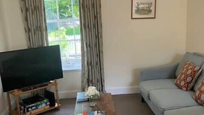 A living room with a sofa, a television on a stand, a coffee table, and a window with curtains. - No 2 Stable Yard, Wemyss Castle Estate (Kirkcaldy)