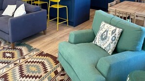 Een moderne woonkamer met een bank, een groene fauteuil en een kamerkleed met dessin.