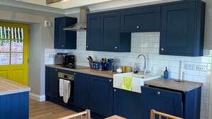 Een moderne keuken met donkerblauwe kastjes, een houten tafel en een felgele deur.