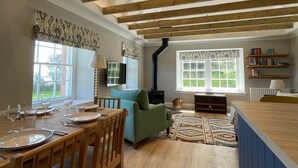 Een ruime woonkamer met houten plafond, een eettafel gedekt met borden en glazen, een bank en een open haard.