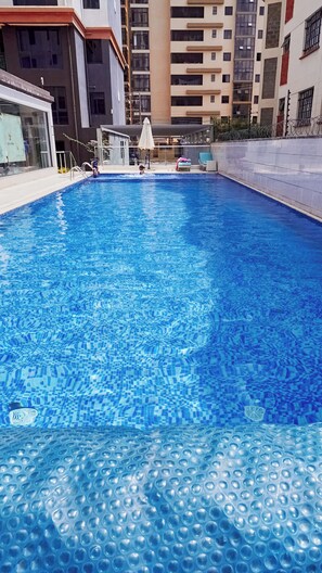 Una piscina con suelo de baldosas, rodeada por un edificio de gran altura con balcones.