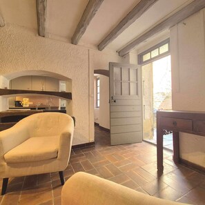 A room with a sofa, a kitchen area with a coffee machine, and a door leading to an outdoor area. - Authentic stone house in the heart of a medieval village · sea 20 min away (Lama)