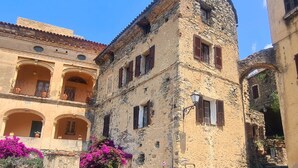 A stone building with arched windows and balconies, surrounded by cobblestone streets and vibrant flowers. - Authentic stone house in the heart of a medieval village · sea 20 min away (Lama)