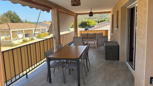 Un patio techado al aire libre con una mesa y sillas, una lámpara colgante y vistas a casas vecinas.