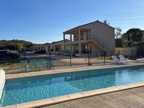 A poolside view of a two-story building with a balcony, a fenced area with lounge chairs, and a clear blue sky. - Ô Gorges-a 5-minute walk from the river and the Ardèche gorges (Vallon-Pont-d'Arc)