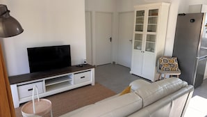 Una sala de estar con sofá, televisión, mueble y refrigerador.
