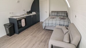 Un dormitorio compacto con cama, sofá, kitchenette y techo curvo.