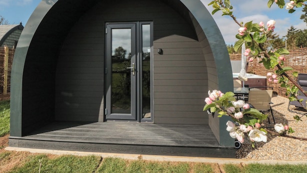 Una estructura moderna, de color oscuro y forma arqueada, con puerta de vidrio y un pequeño porche.