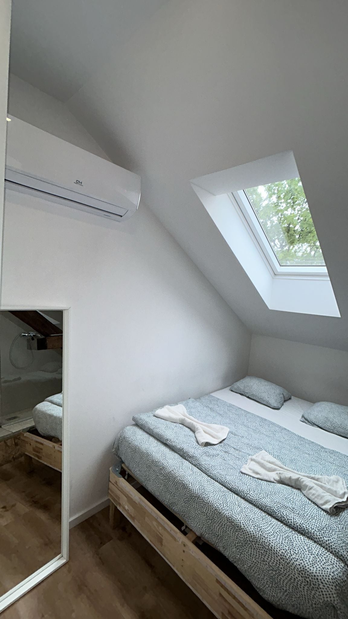 Ein Schlafzimmer mit schrägen Wänden, einem Oberlicht, einem Bett mit gemusterten Betttextilien und Holzboden.