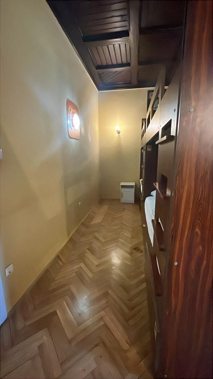 Un estrecho pasillo con suelo de madera, un armario blanco pequeño y una puerta de madera.