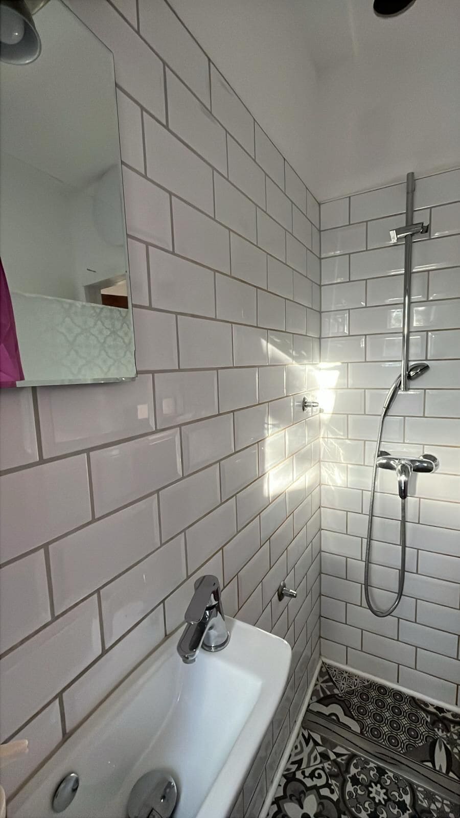 Ein Badezimmer mit weißen Fliesen, einer weißen Badewanne, einer Dusche inklusive Duschkopf und einem Spiegel.