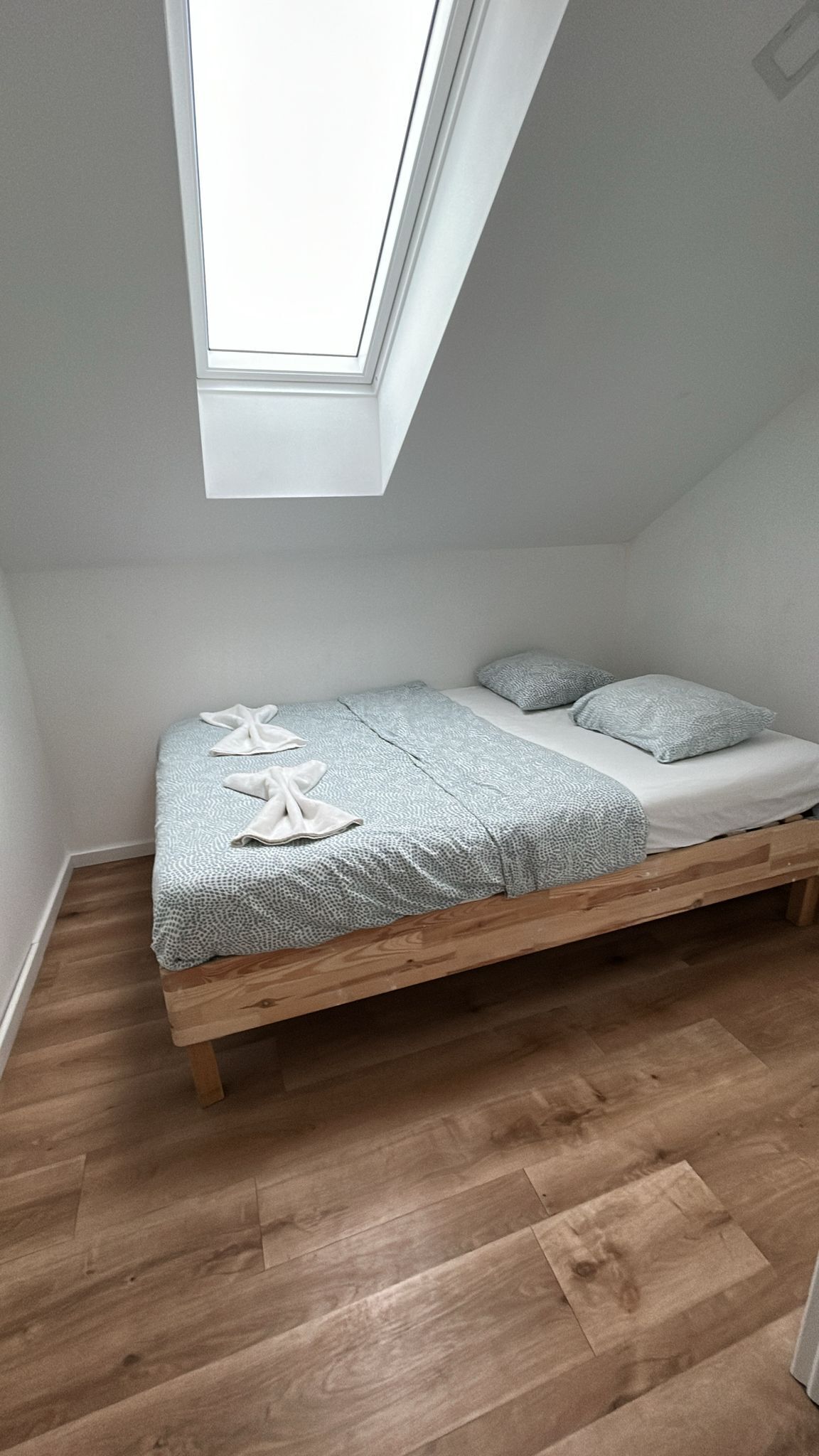 Uma cama de solteiro com estrutura de madeira, claraboia e colcha estampada.