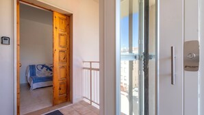 Een hotelkamer met een houten deur, een balkon met een glazen deur en uitzicht op gebouwen.
