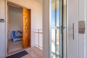 A hotel room with a wooden door, a balcony with a glass door, and a view of buildings outside.