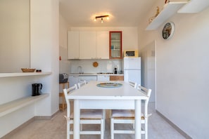 A compact kitchen with white cabinets, a microwave, and a dining table with chairs.